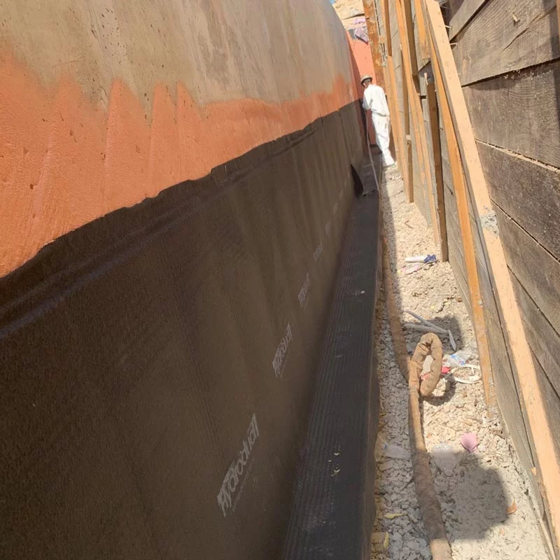 a worker inside a trench applying waterproofing to a wall